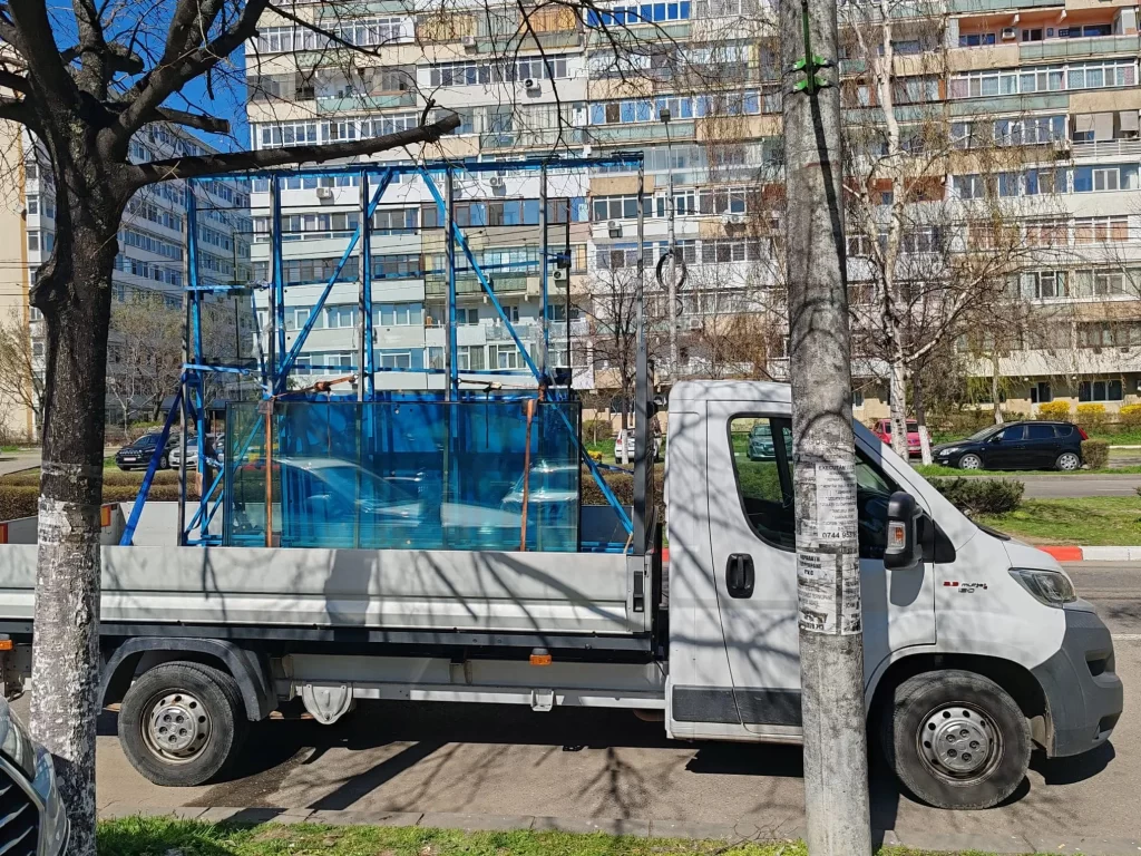 Autoutilitara Fiat Ducato de culoare alba , pe care sa scrie textul: 'Ovi Trans ' , cu usile din spate deschise , iar in spatele ei se vede cum un stivuitor incarca un palet cu marfa