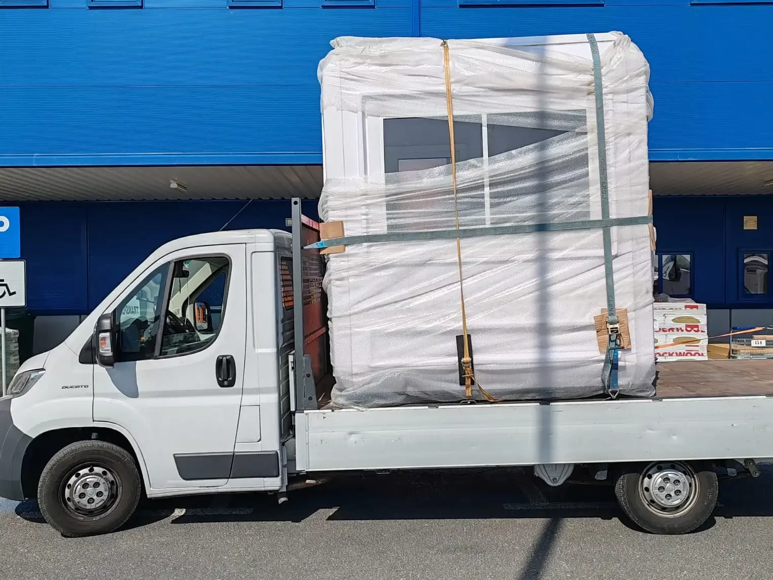 Autoutilitara Fiat Ducato de culoare alba , pe care sa scrie textul: 'Ovi Trans ' , cu usile din spate deschise , iar in spatele ei se vede cum un stivuitor incarca un palet cu marfa